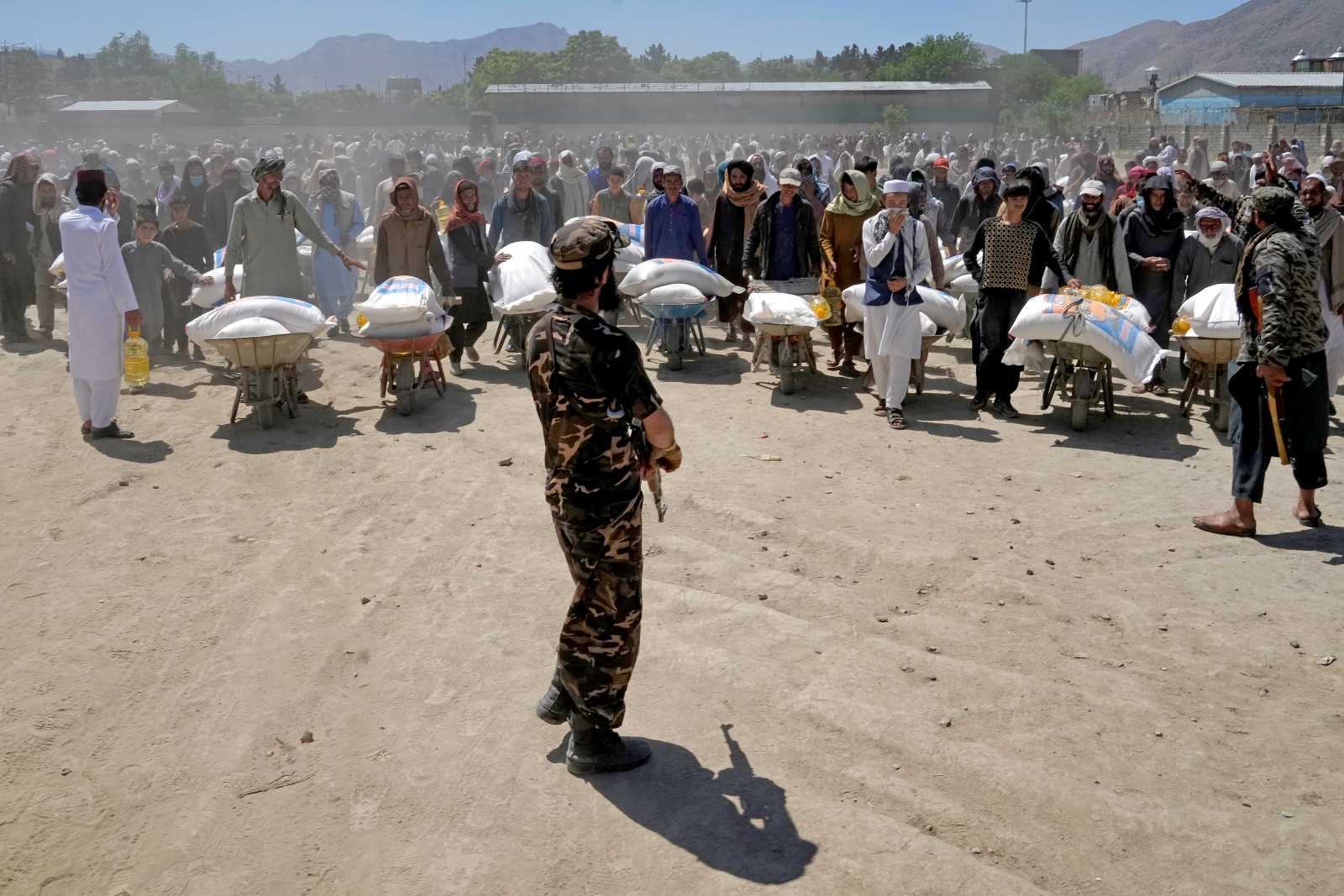 A Taliban fighter stands guard as people receive food rations from China in Kabul, Afghanistan.