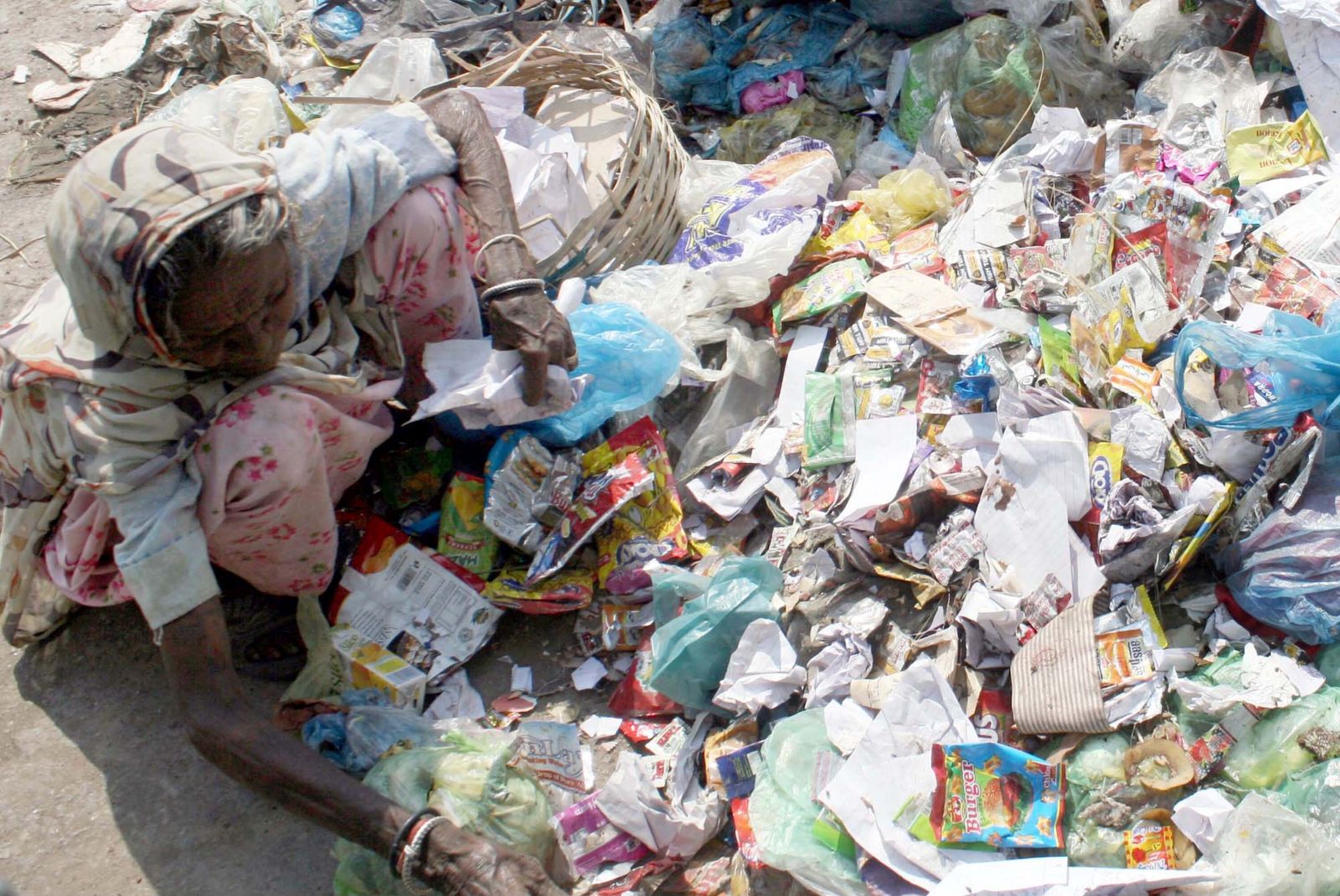 Mittellose Frau sortiert Plastikmüll auf einer Straße in Karachi.