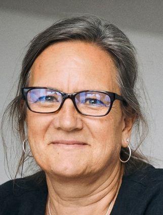 Close-up portrait of a woman wearing glasses with hair pulled back, slightly smiling against a neutral background.