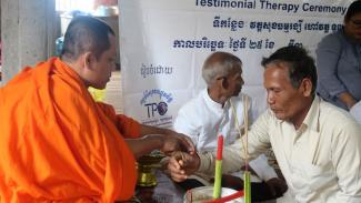 A monk ties a red ribbon around the arm of a Cambodian man for protection purposes. The red ribbon also stands for prosperity and happiness.